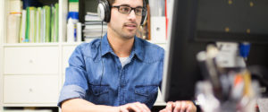 A student wearing headphones as he works at his computer.