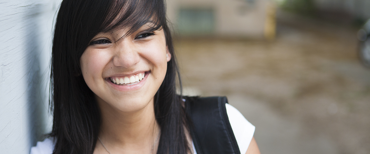 A smiling student leaning against a wall.