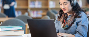 An image of student wearing headphones as she works at her laptop.