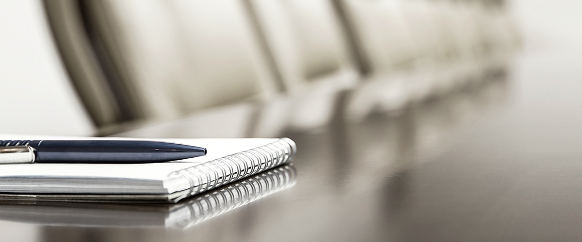 An image of a pen and notepad on a board room table.