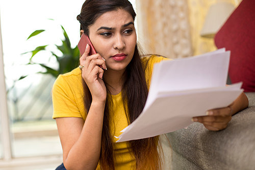 Image of a young woman talking on her cellphone and looking over paperwork.