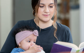 A student reading a book while holding her baby.