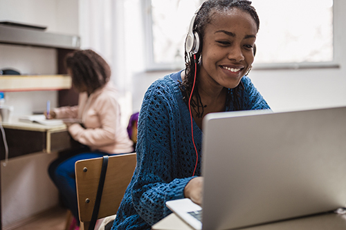 An image of a woman working on her laptop with headphones.