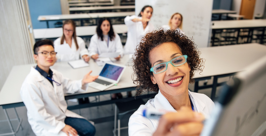 An image of science students working at a whiteboard and on laptops.